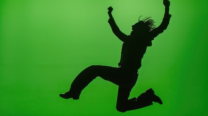 Silhouette of a carefree person jumping in celebration, isolated on a green background, conveying freedom.