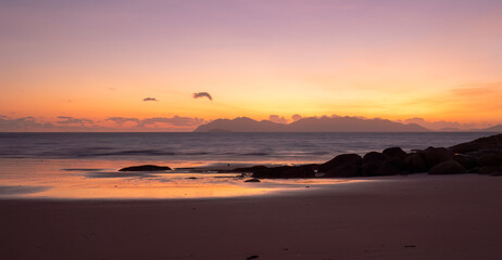 Glorious colors at sunrise with silhouetted rocks and reflections in the water on the beach at Rose Bay in Bowen a popular tourist destination in the Whitsunday region of Queensland, Australia.