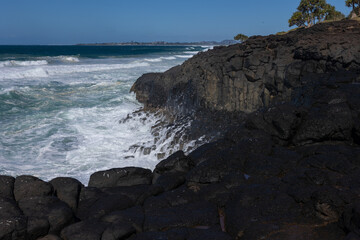 The foam of a huge wave on a rough sea day runs off the rocks after breaking against the hexagonal columnar basalt rocks of the high cliffs at Fingal Head in New South Wales, Australia.