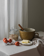 Baking ingredients - flour, eggs, butter, ceramic bowl on the kitchen table. Cozy house concept