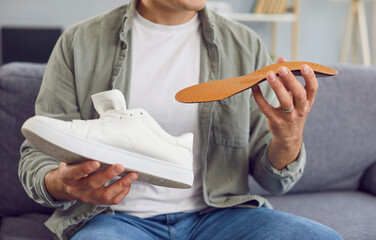 Portrait of a cropped young man wearing casual clothes sitting on sofa at home and holding an...