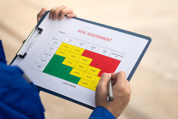 An engineer is using a pen to checking on the safety risk assessment with color matrix form to...