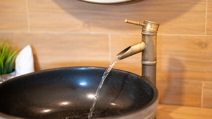Luxury designed brass material faucet with water flowing into the ceramic sink. Interior decoration and household equipment object, close-up.