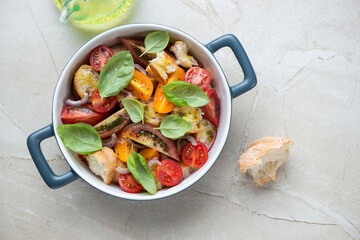 Serving pan with italian traditional panzanella salad, above view on a beige stone background, horizontal shot