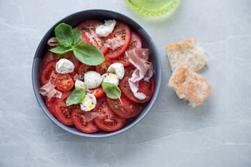 Italian traditional caprese salad served with torn prosciutto on a grey granite background, horizontal shot, view from above