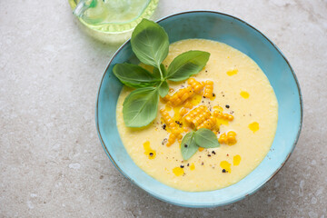 Turquoise bowl with sweet corn gazpacho on a beige stone background, horizontal shot, elevated view