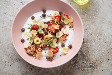Breakfast yogurt bowl with strawberry, granola and flakes, horizontal shot on a beige granite background, high angle view