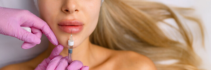 Injection procedure for lip augmentation, close-up. The cosmetologist slowly and carefully injects...