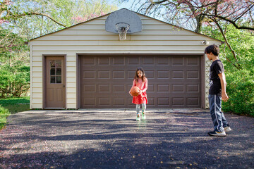 Two children play driveway basketball together in spring