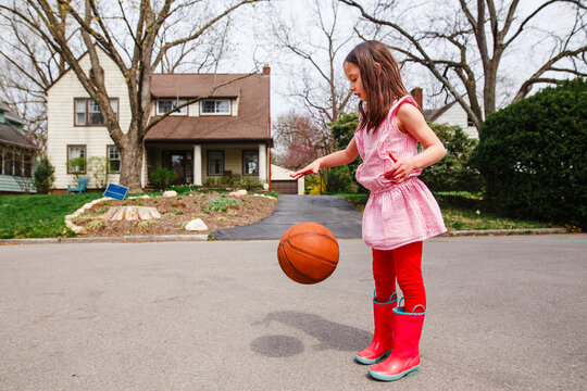 A small girl with rainbows dribbles a basketball in street