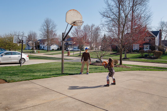 Father and daughter play basketball in driveway together