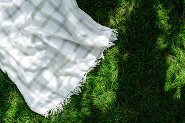 White picnic blanket on a green grass from top view
