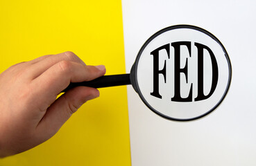 Hand holding magnifying glass over FED abbreviation on yellow and white background