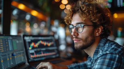 Obraz premium Focused Businessman Analyzing Stock Market Data on Laptop in Modern Office During Evening, Remote Work Concept