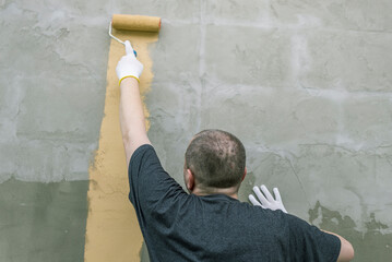 A man meticulously paints a concrete wall with a yellow roller, creating a straight, smooth line....