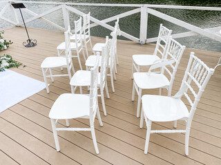 A neat row of pristine white chairs has been carefully arranged on a beautifully finished wooden deck, creating an inviting space for guests to sit and enjoy the surroundings