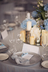 banquet table is decorated with plates, cutlery, glasses, candles and flower arrangements. blue and white flowers decorate the table. 