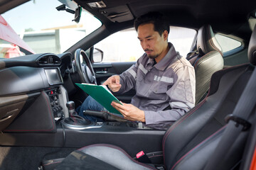 A mechanic in work uniform with a document clipboard, inspect a car coming for maintenance at a...