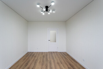 Obraz premium The room is completely empty, featuring a polished wooden floor, pristine white walls, and an elegant chandelier hanging from the ceiling above, creating a unique atmosphere