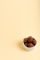 Shelled macadamia nuts in a in small white ceramic plate on a beige background. Tasty and healthy macadamia nuts. Healthy snack. 