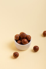 Shelled macadamia nuts in a in small white ceramic plate on a beige background. Tasty and healthy macadamia nuts. Healthy snack. 