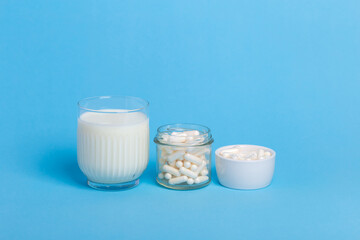 Many lactase tablets in small containers and a glass of milk containing lactose on a blue background. lactase tablets for assimilation of lactose from dairy products. Lactose intolerance.