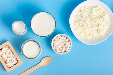Many lactase tablets, yogurt containing lactose, milk, cottage cheese and a wooden spoon from above on a blue background. Lactase enzyme for assimilation of lactose from dairy products. Rustic style