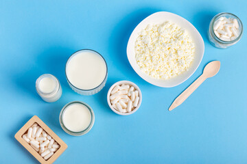 Many lactase tablets, yogurt containing lactose, milk, cottage cheese and a wooden spoon from above on a blue background. Lactase enzyme for assimilation of lactose from dairy products. Rustic style