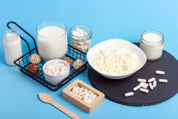 Lactase tablets, yogurt containing lactose, milk, cottage cheese and a wooden spoon on a blue background. Lactase enzyme for assimilation of lactose from dairy products. Rustic style