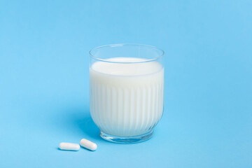 Lactase tablets and a glass of milk containing lactose on a blue background. lactase tablets for assimilation of lactose from dairy products. Lactose intolerance. Enzymes for improving quality of life