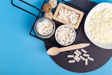 Many lactase tablets, cottage cheese and a wooden spoon on a black round stone desk on a blue...