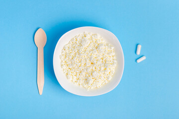 Lactase tablets, cottage cheese containing lactose and a wooden spoon from above on a blue background. lactase tablets for assimilation of lactose from dairy products. Lactose intolerance. 
