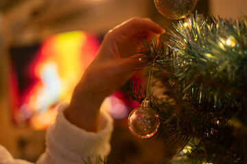 Chica colgando una bola de color transparente en su árbol de Navidad. Momento mágico en casa. Tradición y cultura.  © jordirenart