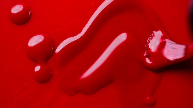 Red nail polish drops, manicure concept. Spilled uv gel, enamel, varnish with brush on red color background, splash. Beauty salon, nail care product. Nail art. Top view, fashion backdrop. Slow motion 
