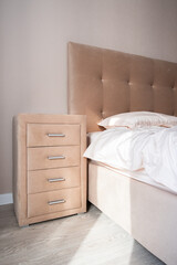 Beige dresser with four drawers near the bed. Well organized bedroom in natural light.