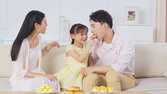 Happy family of three sitting on the sofa enjoys a meal eating mooncakes together while celebrating the Mid-Autumn Festival
