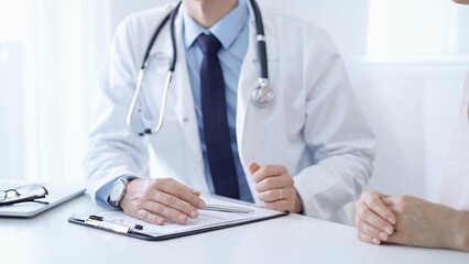 Doctor and a patient. The physician, wearing a white medical coat over a blue shirt and tie, gesturing with his hands during a consultation in the clinic. Medicine concept