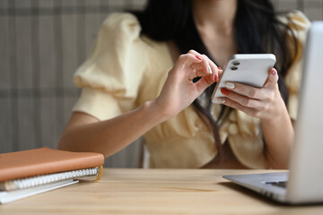 Close up of young woman typing text message on mobile phone while sitting at office desk