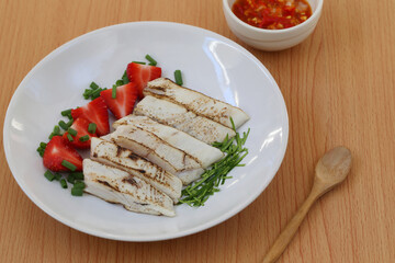 King mackerel aburi arranged on a white plate with strawberries and chopped ​​onions served with seafood dipping sauce.