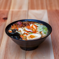 Ramen dish served on a black bowl. Wooden table, Japanese cuisine.