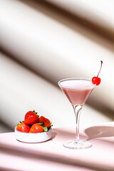 Delicious summer cocktail with vodka, liqueur, cream, strawberries and ice  with cocktail cherry. Beige background, hard light