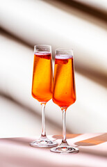 Strawberry festive cocktail drink with dry champagne, fruit puree and ice in glasses. Beige pink background, hard light