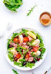 Tasty salad with tuna, tomatoes, eggs, beans, lettuce and olives with mustard dressing on white background, top view