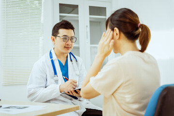 Fototapeta premium A male Asian pediatrician in a white lab coat sits at his desk, warmly greeting a middle-aged pregnant woman for a prenatal consultation, offering care and support in a clinical setting.