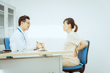 Obraz premium A male Asian pediatrician in a white lab coat sits at his desk, warmly greeting a middle-aged pregnant woman for a prenatal consultation, offering care and support in a clinical setting.