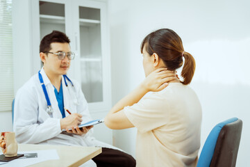 A male Asian pediatrician in a white lab coat sits at his desk, warmly greeting a middle-aged pregnant woman for a prenatal consultation, offering care and support in a clinical setting.