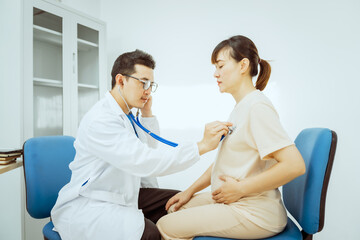 Obraz premium A male Asian pediatrician in a white lab coat sits at his desk, warmly greeting a middle-aged pregnant woman for a prenatal consultation, offering care and support in a clinical setting.