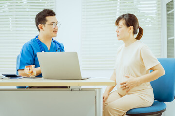 Obraz premium A male Asian pediatrician in a white lab coat conducts a prenatal checkup for a middle-aged pregnant woman, focusing on maternal and fetal health, offering expert care and guidance.