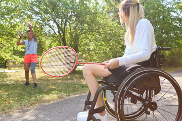Woman in wheelchair playing badminton with friend outdoors on a sunny day