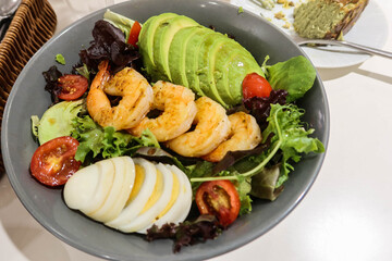close up of healthy salad with avocado, prawns, shrimps, boiled egg, cherry tomato, vegetables in a blue bowl
